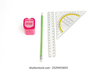 A pencil, a ruler, and a pencil sharpener are placed on a white surface. The pencil sharpener is pink and has a small container for pencil shavings. The ruler is white - Powered by Shutterstock