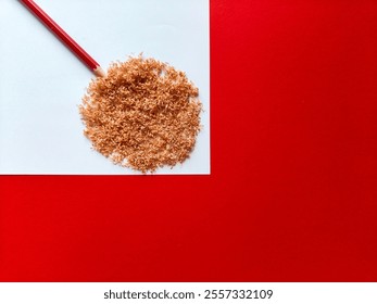 Pencil shavings rolled into a circle shape with a red pencil as stem on white paper, upper left corner of red background. - Powered by Shutterstock