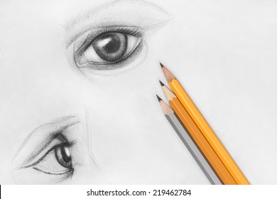 Pencil sketch of female eyes on white paper with pencils