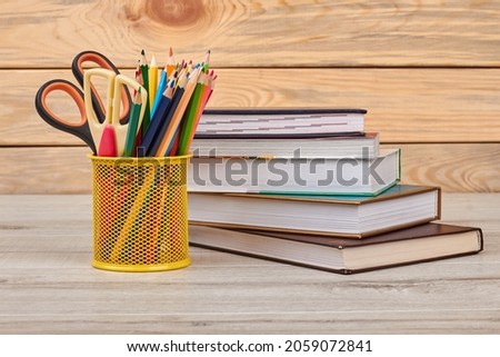 Pencils in metal holder and stack of books.