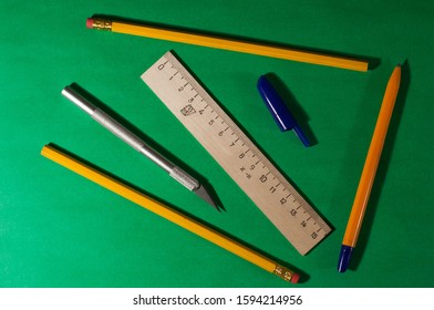 Pencils, Pen And Cap, Scalpel And Wooden Ruler On A Green Background. Close-up.