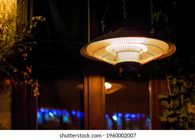 Pendant Heater Glowing With Warm Light And Radiating Warmth By The Window Of The Backyard Terrace Night Scene.