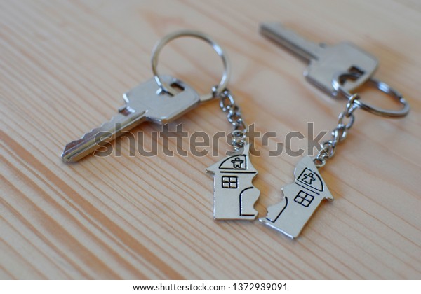 Pendant of key ring in shape\
of house divided in two parts on wooden background, closeup view.\
Dividing house when divorce, division of property and real\
estate.\
