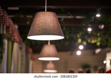 Pendant lamps over tables in city cafe, evening lighting restaurant. Beige fabric lampshades with low dimmed warm light. Modern cozy interior, country style pendant lighting
