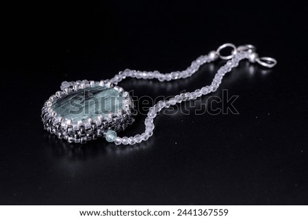 A pendant made of processed aquamarine, a precious rare gemstone of pale blue color. Smooth, radiant. Against a dark background. A jewelry piece for women and men.
