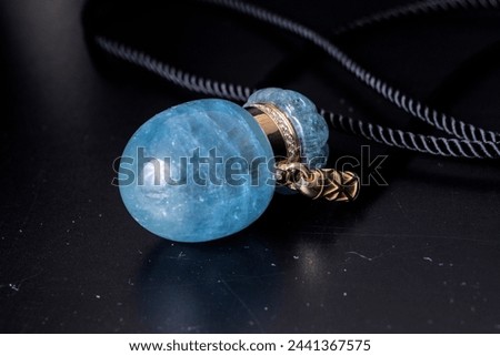 A pendant made of processed aquamarine, a precious rare gemstone of pale blue color. Smooth, radiant. Against a dark background. A jewelry piece for women and men.