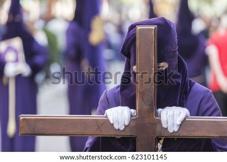 Penitent dressed in purple tunic of velvet resting on wooden cross during atonement station on Holy Week, Andalusia, Spain