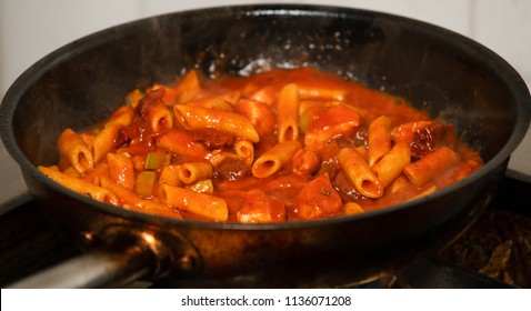Penne Pasta Cooking In Fresh Homemade Tomato Sauce With Zucchini And Sun Dried Tomatoes - Real Food Cooking Concept. Delicious Corn Pasta Simmering In A Rustic Pot, Extreme Close-up Background.