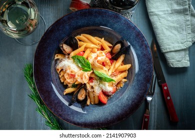 Penne Pasta With Seafood In A Plate On The Table. Italian Pasta Dish With Mussels, Squid, Tomatoes And Parmesan, Close Up
