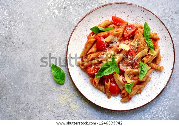 Penne pasta with tomato in red sauce on a white\
plate over light grey slate, stone or concrete background.Top view\
with copy space.