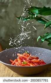 Penne Pasta With Tomato Sauce And Basil In A Gray Plate. Parmesan Cheese Is Falling.