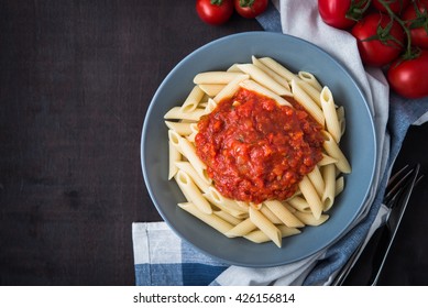 Penne Pasta With Tomato Sauce On Dark Wooden Background Top View. Italian Cuisine.