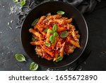 Penne pasta with tomato sauce, parmesan cheese and basil on dark background. Top view with copy space.