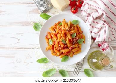 Penne pasta with tomato sauce, parmesan cheese and basil on wooden table. Top view with copy space. - Shutterstock ID 2128096847