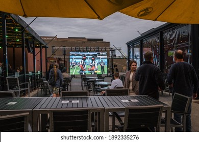 Pensacola, FL, US-December 6, 2020: Bar With Outdoor Seating During Covid-19 Pandemic. Patrons Are Socially Distancing And Some Are Masked While Watching A Football Game On A Large Screen Television.