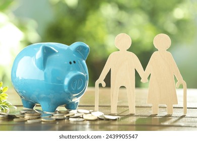 Pension savings. Figure of senior couple, piggy bank and coins on wooden table outdoors - Powered by Shutterstock