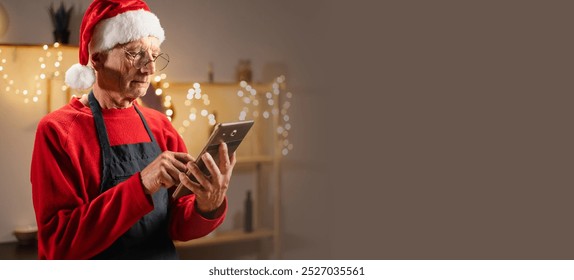 Pensioner cooking pastries in the kitchen for Christmas reads the recipe online using a digital tablet while standing in the kitchen. Banner, space for text - Powered by Shutterstock