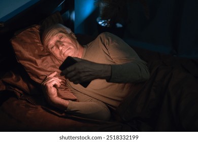 Pensioner old man uses mobile phone lying in his bed at night suffering from insomnia and mobile addiction. Copy space - Powered by Shutterstock