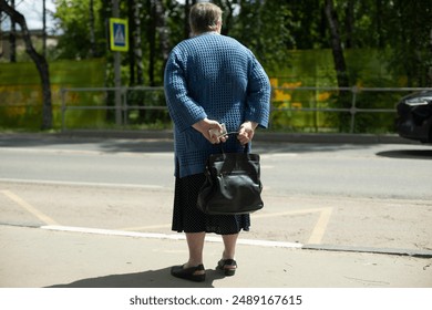 Pensioner is waiting for bus on road. Grandma with bag. Elderly woman in city. Waiting for transport in city. - Powered by Shutterstock