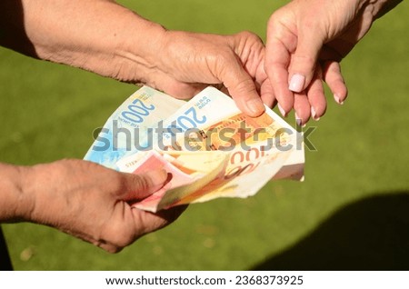 A pensioner woman holds new Israeli shekel banknotes and an Israeli citizen passport in her hands. Concept pension, social assistance, budget, old-age benefits, new repatriate 