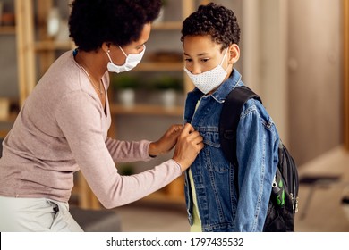 Pensive African American boy and his mother wearing protective face masks while getting ready to go back to school during coronavirus epidemic.  - Powered by Shutterstock