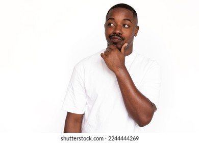 Pensive African American man touching chin. Portrait of unsure young male model with short hair in white T-shirt looking away, pouting lips with hand on chin. Advertisement, contemplation concept