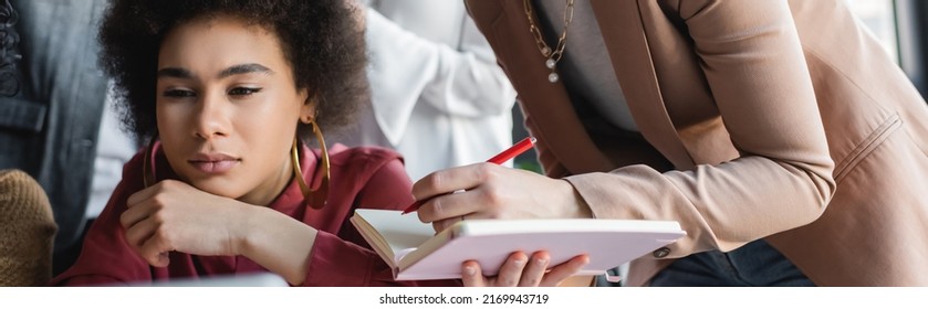 Pensive African American Woman Thinking Near Colleague With Notebook In Ad Agency, Banner