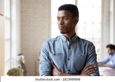Pensive African American young male employee stand in office look in window distance thinking, thoughtful biracial millennial man worker pondering planning, business vision concept