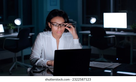 Pensive African-American executive read information on laptop in dark empty office. Businesswoman work on computer late in modern office - Powered by Shutterstock