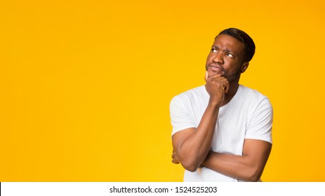Pensive Afro Man Thinking Touching Chin Standing Over Yellow Studio Background. Panorama With Free Space
