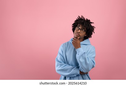 Pensive Afro teen guy touching his chin, thinking over something on pink studio background, copy space. Puzzled teenager deep n thought, making choice or decision, imagining or daydreaming