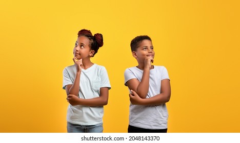 Pensive afro-american boy and girl posing on yellow studio background, black brother and sister thinking about something, touching chins and looking at copy space, panorama. Kids lifetime