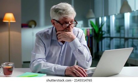 Pensive aged man using laptop paying bills online at home. Senior businessman work on computer. Grandfather browsing internet in living room