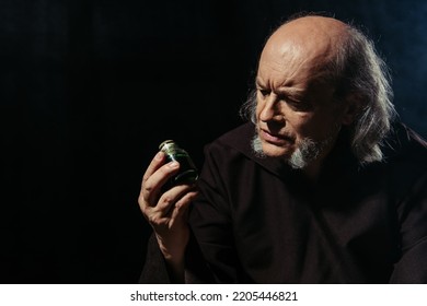 Pensive Alchemist Looking At Jar With Magic Ingredient Isolated On Black