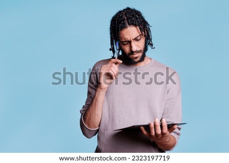 Pensive arab man thinking while holding clipboard and planning. Thoughtful young adult person in doubt reading checklist and touching face with pen with puzzled expression