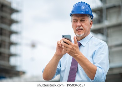 Pensive architect closing his eyes and thinking while using his smartphone