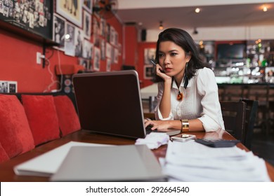 Pensive Asian Bar Owner Using Laptop To Pay Bills Online