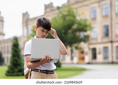 Pensive asian schoolboy looking at laptop outdoors