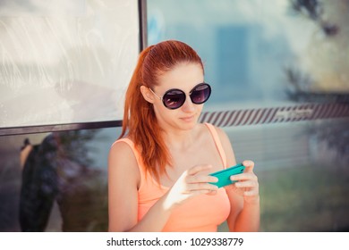 Pensive attractive trendy woman female girl sitting in a bus station using application on smartphone for calling taxi - Powered by Shutterstock