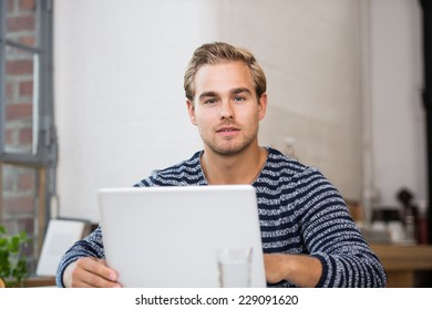 Pensive attractive young young man sitting at his laptop staring at the camera with a serious contemplative expression