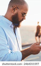 Pensive bearded guy installing application on smartphone via good internet connection on street, male hipster uploading content in social networks blogging via telephone cellular standing outdoors