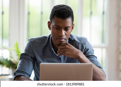 Pensive Biracial Millennial Male Employee Look At Laptop Screen Working In Office, Thoughtful African American Young Man Worker Busy Working On Computer Pondering Over Problem Solution