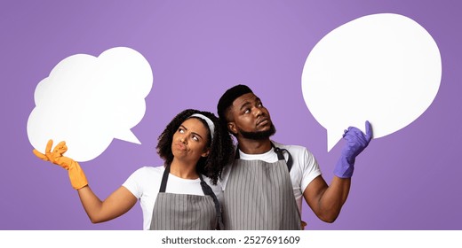 Pensive Black Couple Wearing Aprons And Rubber Gloves Looking At Empty Speech Bubbles Above Their Heads, Copy Space - Powered by Shutterstock