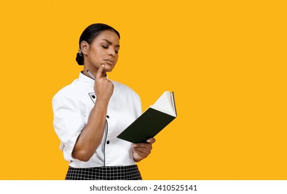 Pensive black female chef reviewing notes in cook book, young african american cook woman with thoughtful expression standing against bright yellow background, symbolizing careful planning of menu - Powered by Shutterstock