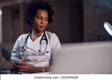 Pensive Black Healthcare Worker Text Messaging On Mobile Phone At Doctor's Office. 