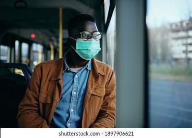 Pensive black man looking through the window and wearing face mask while commuting by bus during coronavirus pandemic. 