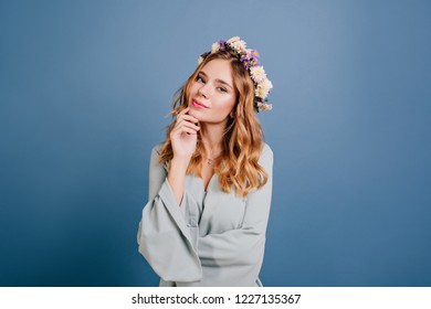 Pensive blonde girl with beautiful eyes posing on dark background. Indoor photo of glad white lady wears circlet of flowers touching her face. - Powered by Shutterstock