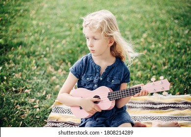 Pensive Blonde Girl Playing Pink Guitar Toy Outdoor. Child Playing Music And Singing Song In Park. Hobby Activity For Children Kids. Authentic Candid Childhood Moment. 