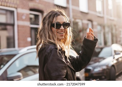 Pensive blonde woman in black leather jacket, black glasses and turn back posing on street background. Outdoor shot of happy hippie lady with two thin braids and wave hair. Boho freedom style - Powered by Shutterstock