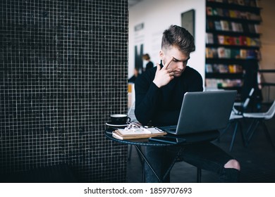 Pensive Broody Man In Black Turtleneck And Ripped Jeans Rubbing Eyebrow While Working On Laptop And Trying To Figure Out Difficult Work Issue